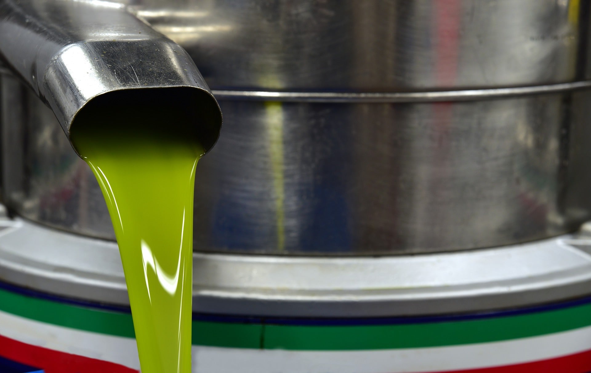 The flow of freshly pressed olive oil from a stainless steel spout during production
