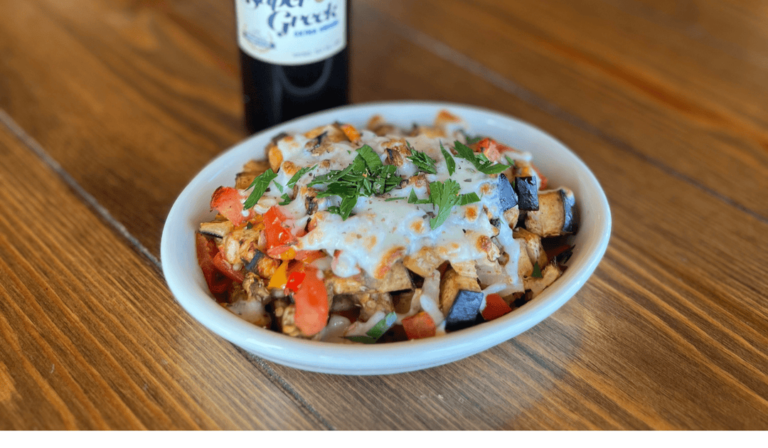 eggplant medley in a white bowl with roma tomatoes, red, yellow and orange bell pepper topped with mozzarella cheese garnished with chopped parsley