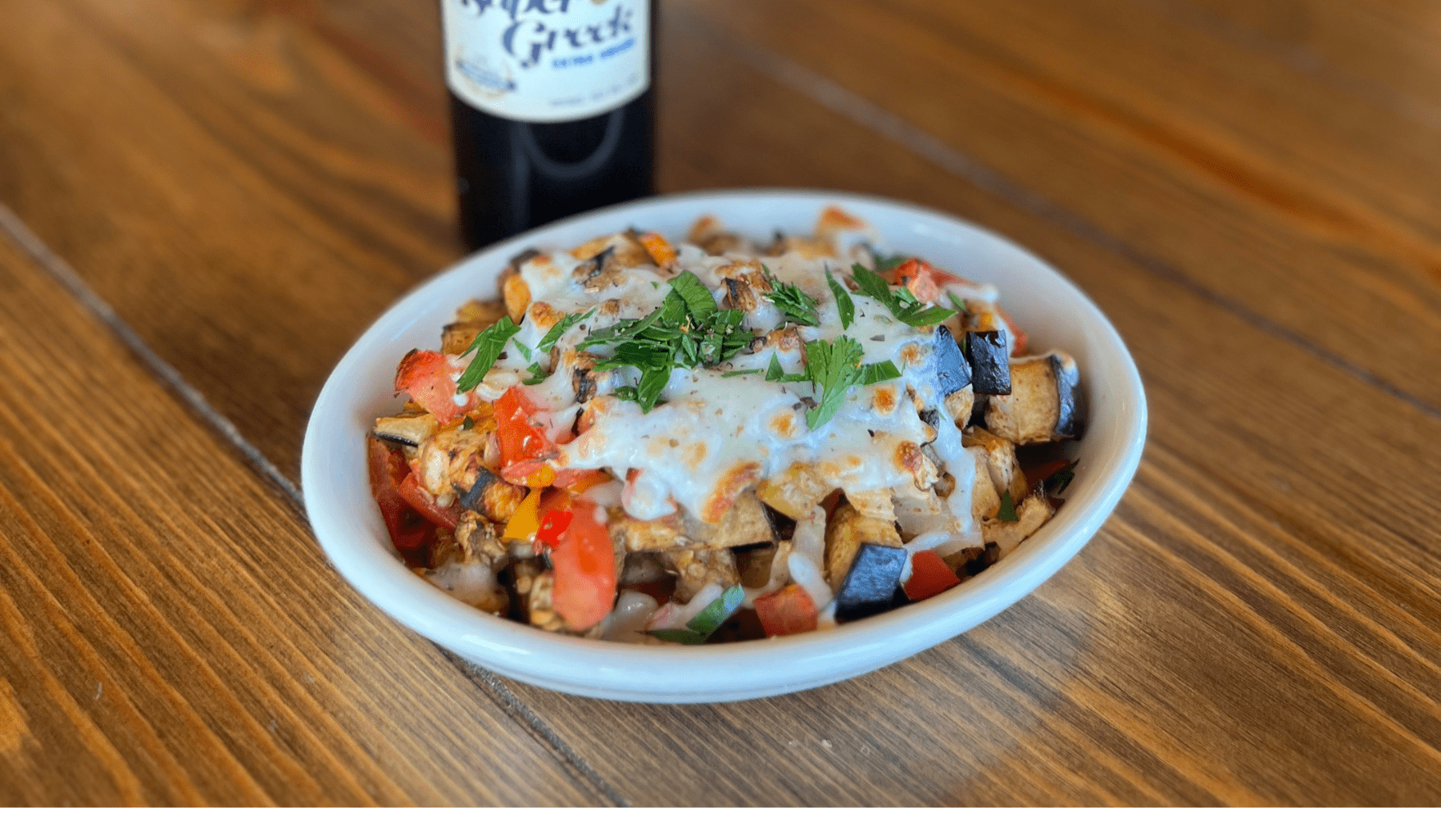eggplant medley in a white bowl with roma tomatoes, red, yellow and orange bell pepper topped with mozzarella cheese garnished with chopped parsley