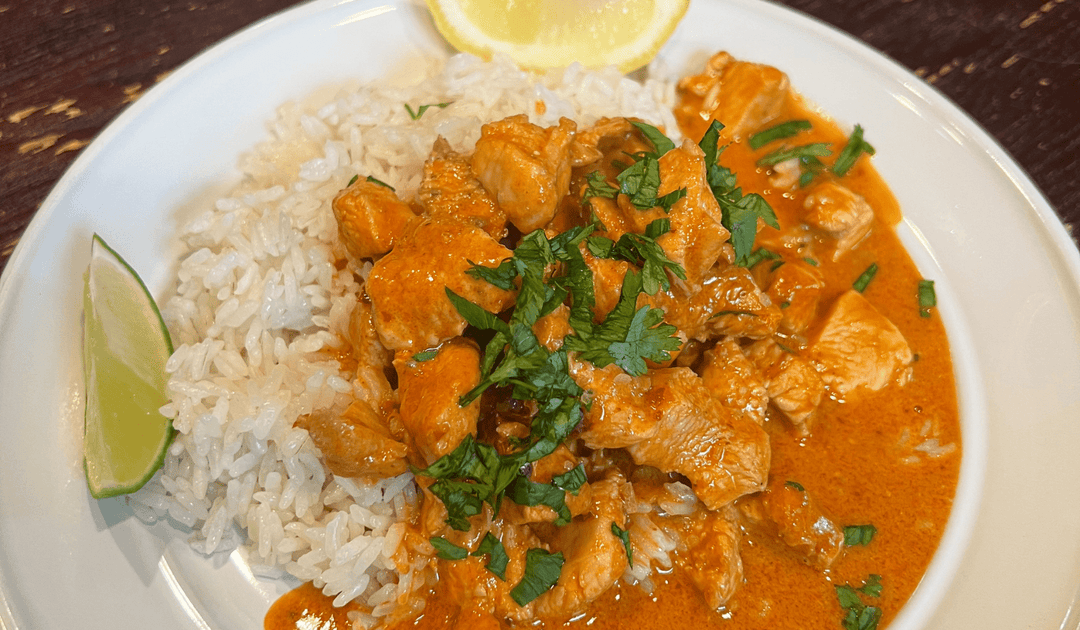 harissa chicken with white rice on a white place garnished with parsley, lime wedge and lemon wedge
