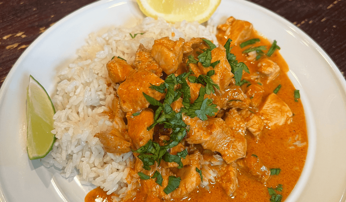 harissa chicken with white rice on a white place garnished with parsley, lime wedge and lemon wedge