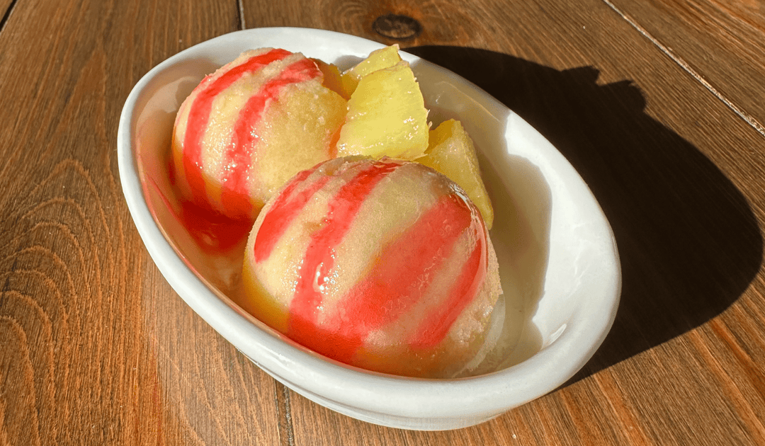 yellow pineapple ginger sorbet in a white ramekin topped with a pink prickly pear balsamic syrup and fresh pineapple pieces