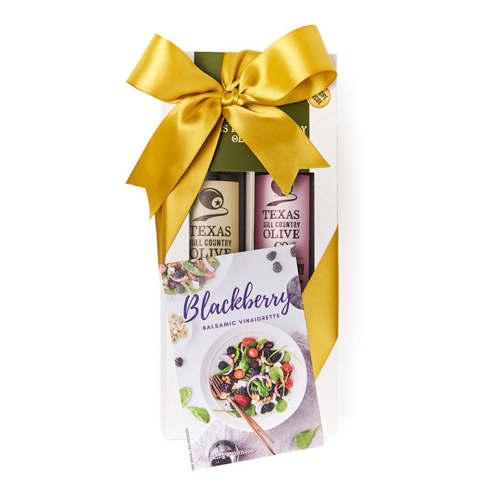 A gift set of three Texas All Country Olive products in a white box tied with a large gold bow, featuring a Blackberry Balsamic vinegar favorite card in front.