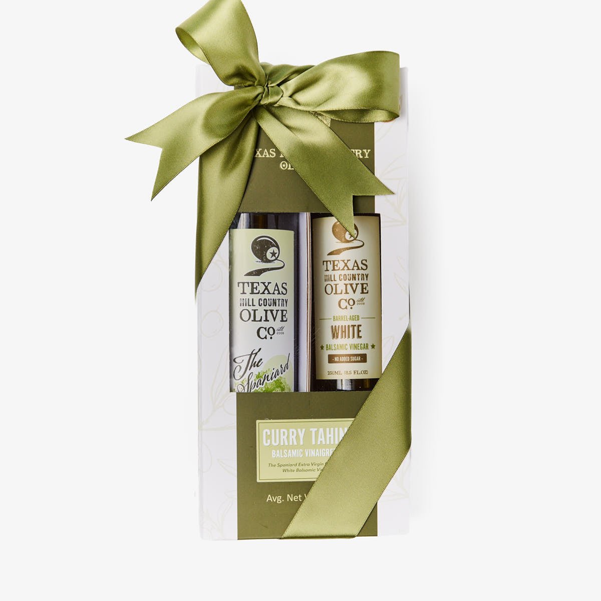 A Texas Olive Company gift set in a clear window box package tied with a large olive green satin bow. The set includes a bottle of The Spaniard Olive Oil and White balsamic 