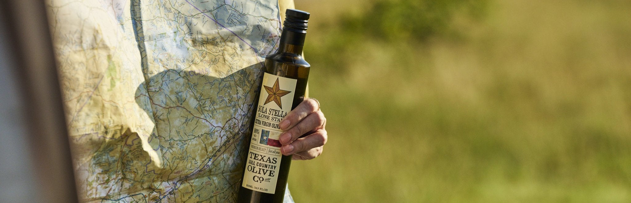 Person holding a bottle of Texas olive oil with a map in the background