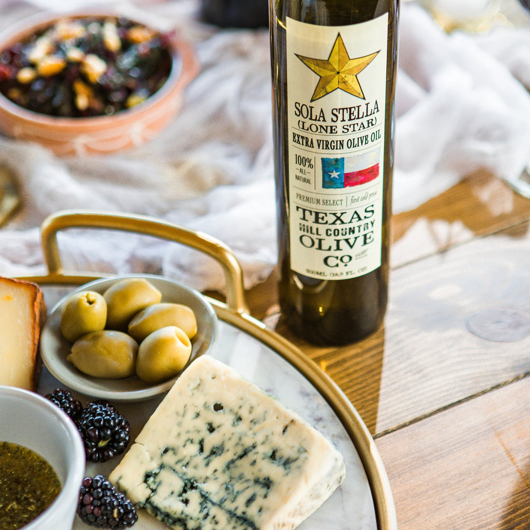 Sola Stella Extra Virgin Olive Oil beside a platter of cheese, green olives, blackberries and dipping oil.