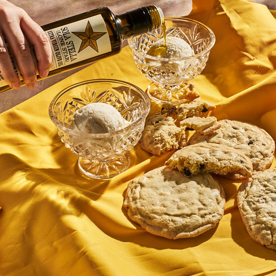 Sola Stella Extra Virgin Olive Oil drizzled over ice cream in glass dessert bowls beside cookies.