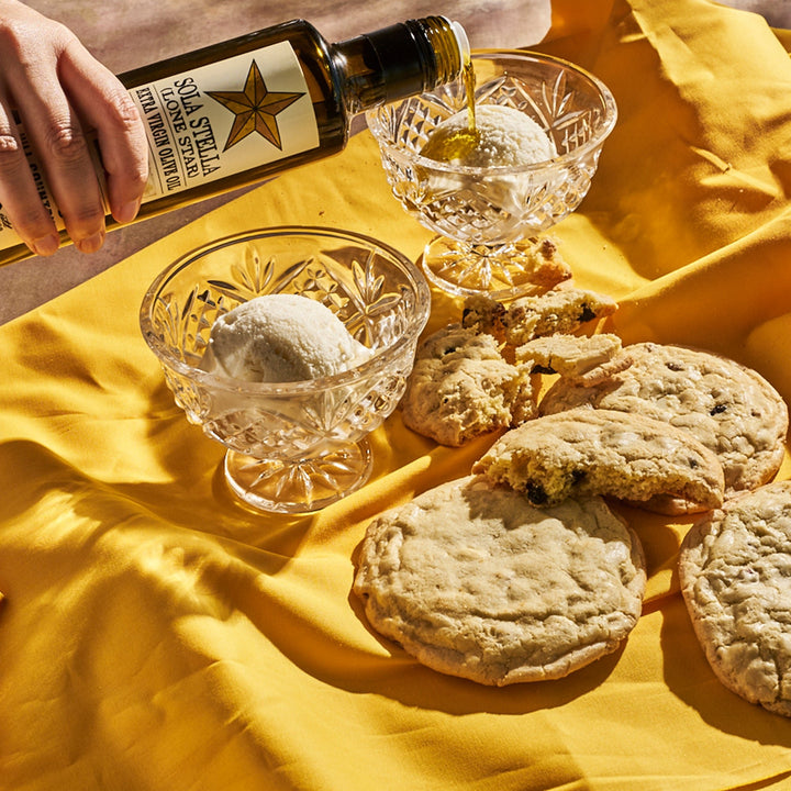 Sola Stella Extra Virgin Olive Oil drizzled over ice cream in glass dessert bowls beside cookies.